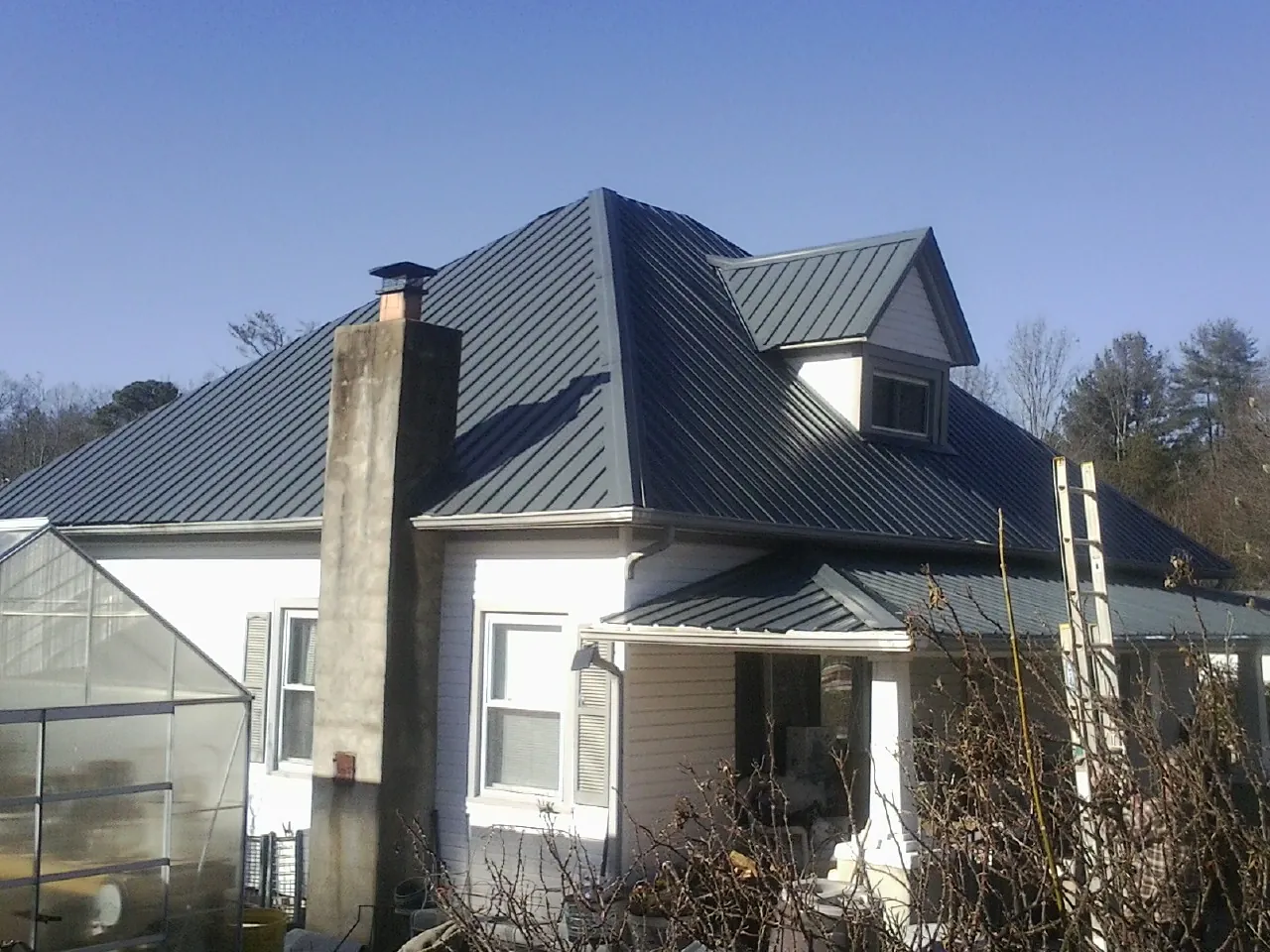 Dark blue standing seam metal roof on a white farmhouse with dormer — Slate & Tile Roof Repair by Roofing Brothers in Brockport