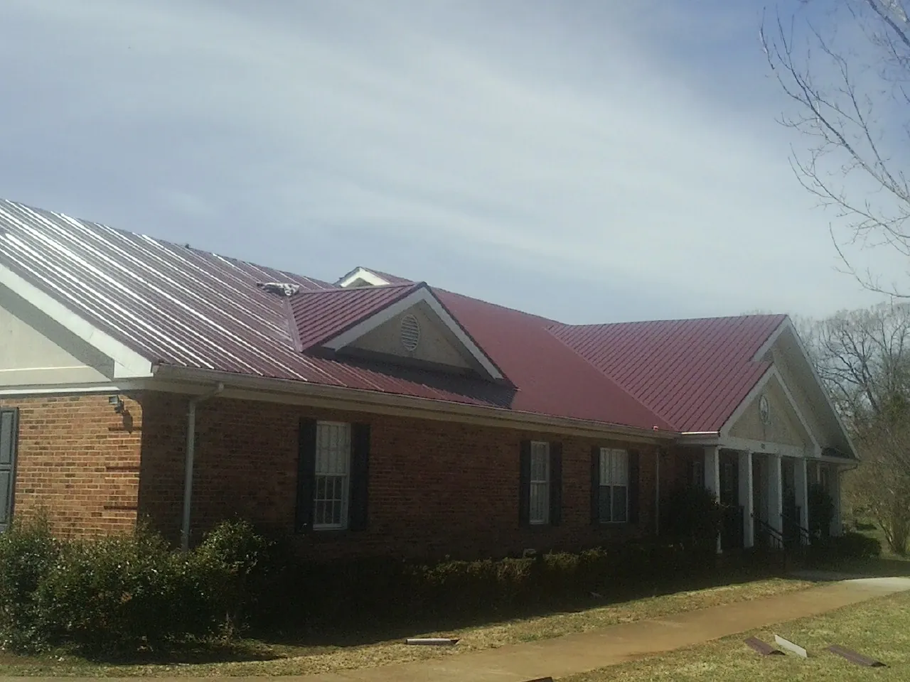Red metal roof with gabled entries on a long brick building, from a Hail Damage Roof Repair job in Brockport