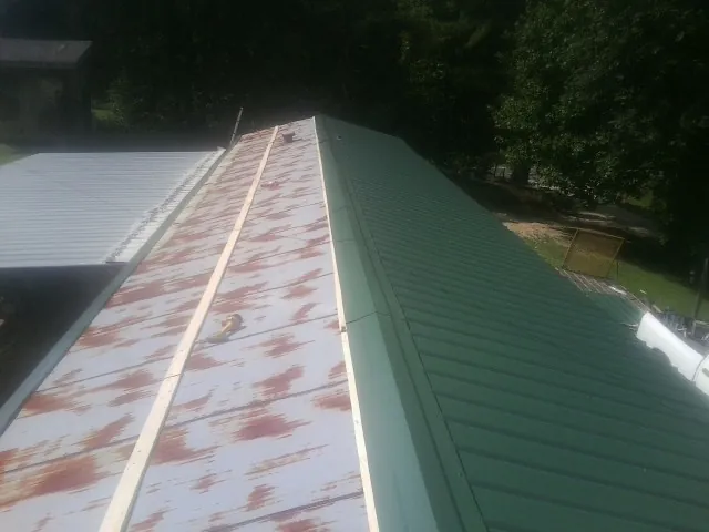Old rusted panels beside newly installed green metal roofing — Wind Damage Roof Repair by Roofing Brothers in Brockport