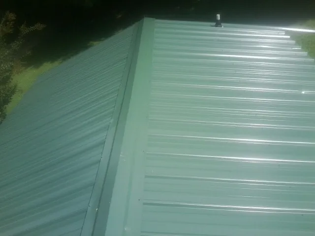 New green metal panels meeting at the ridge of a roof — Flat Roof Repair work by our crew in Brockport