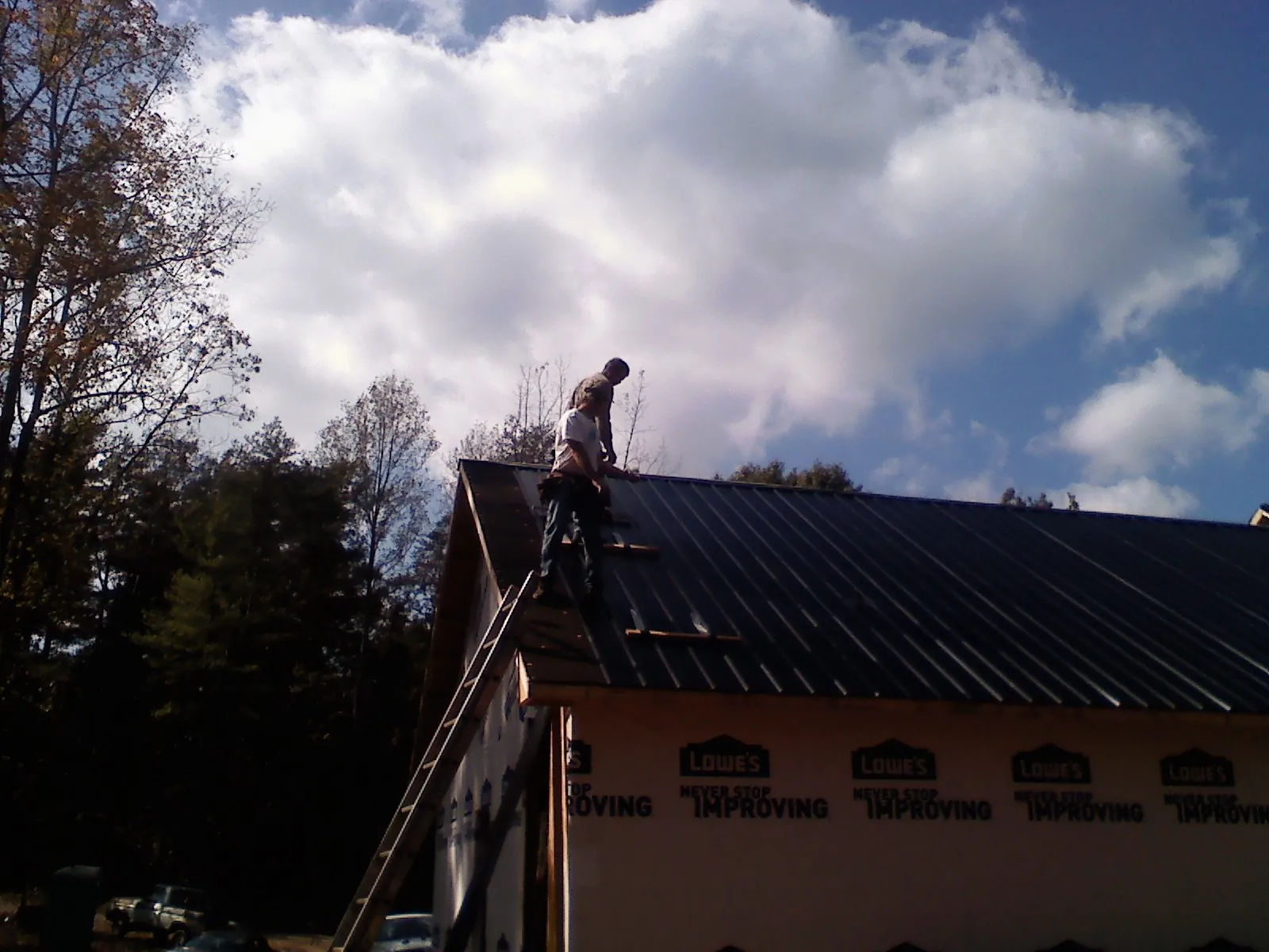 Roofer fastening dark metal panels high against a cloudy sky, from a Roof Inspection job in Brockport