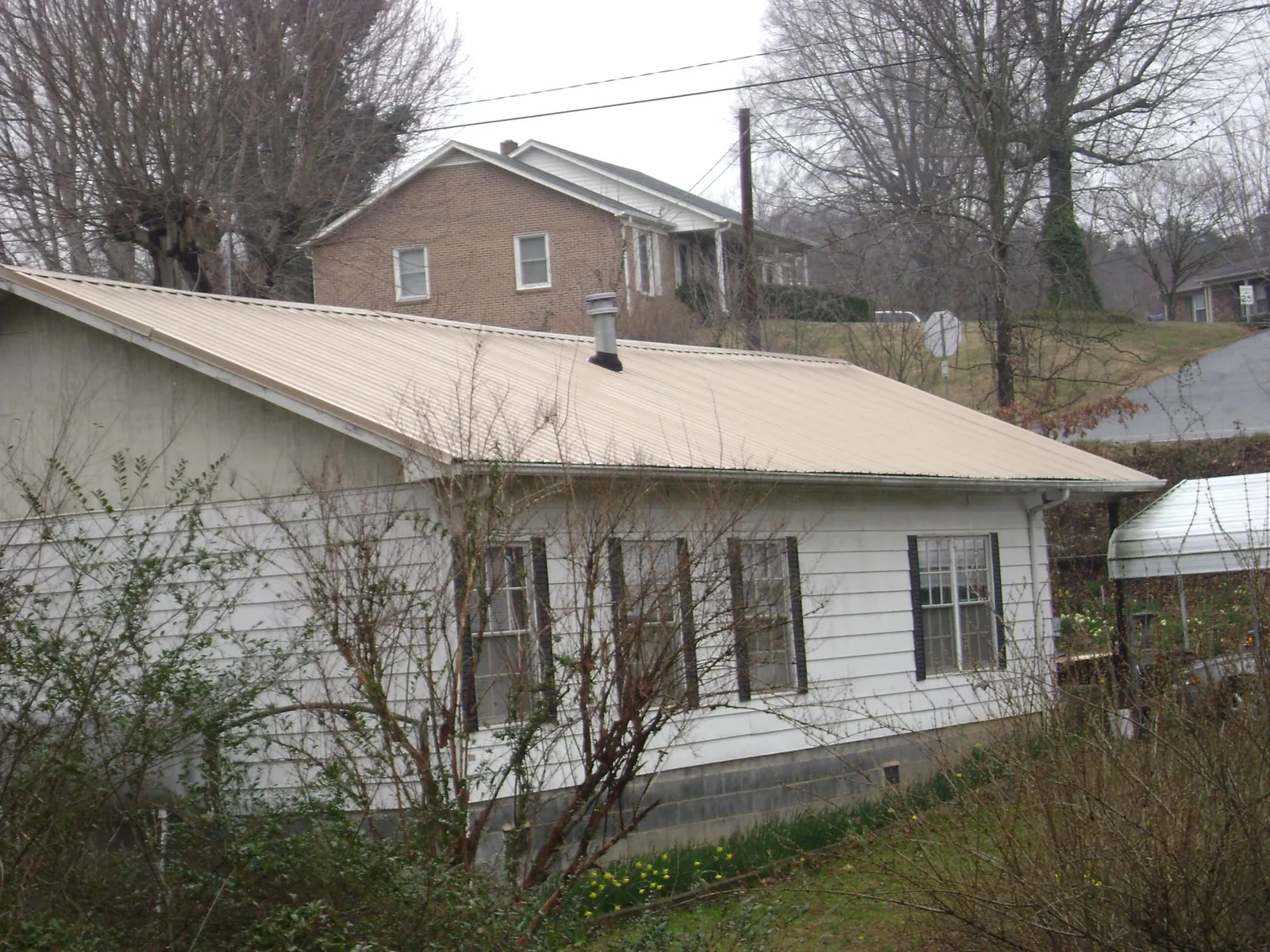 Tan metal roof on a white sided house set into a hillside — Commercial Roofing by Roofing Brothers in Brockport