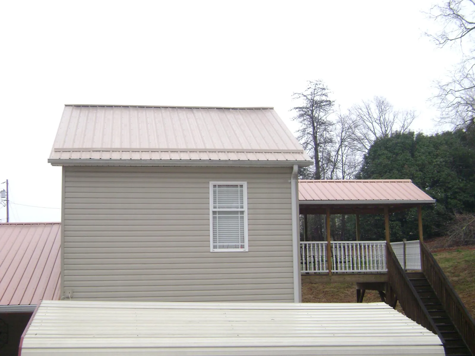 Tan metal roofs on a two story addition and attached porch, from a Roof Replacement job in Brockport
